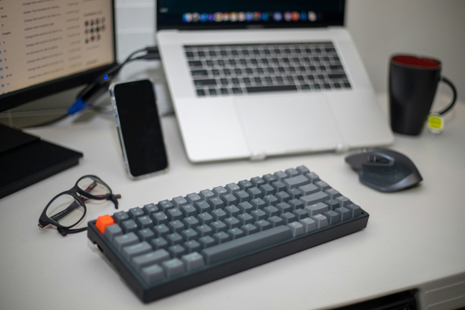  a desk with a laptop, keyboard, glasses, phone, and mouse