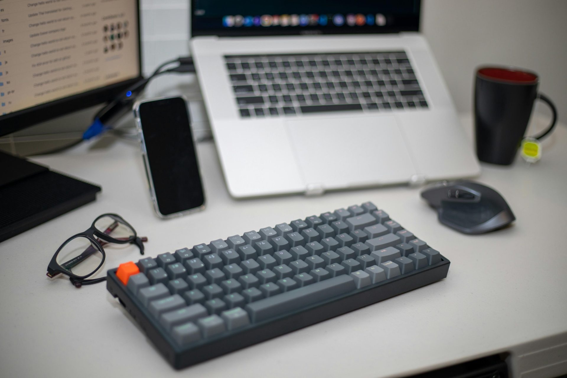 a desk with a laptop, keyboard, glasses, phone, and mouse
